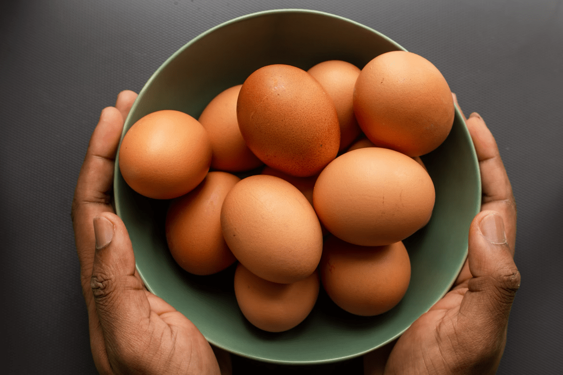 light green bowl with many brown eggs, held by two hands on either side
